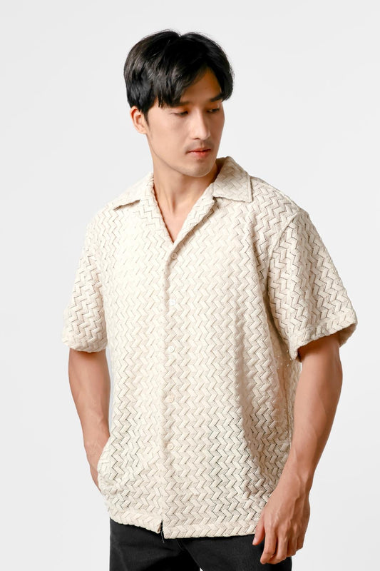 Man wearing a textured cream shirt and black pants on a white background