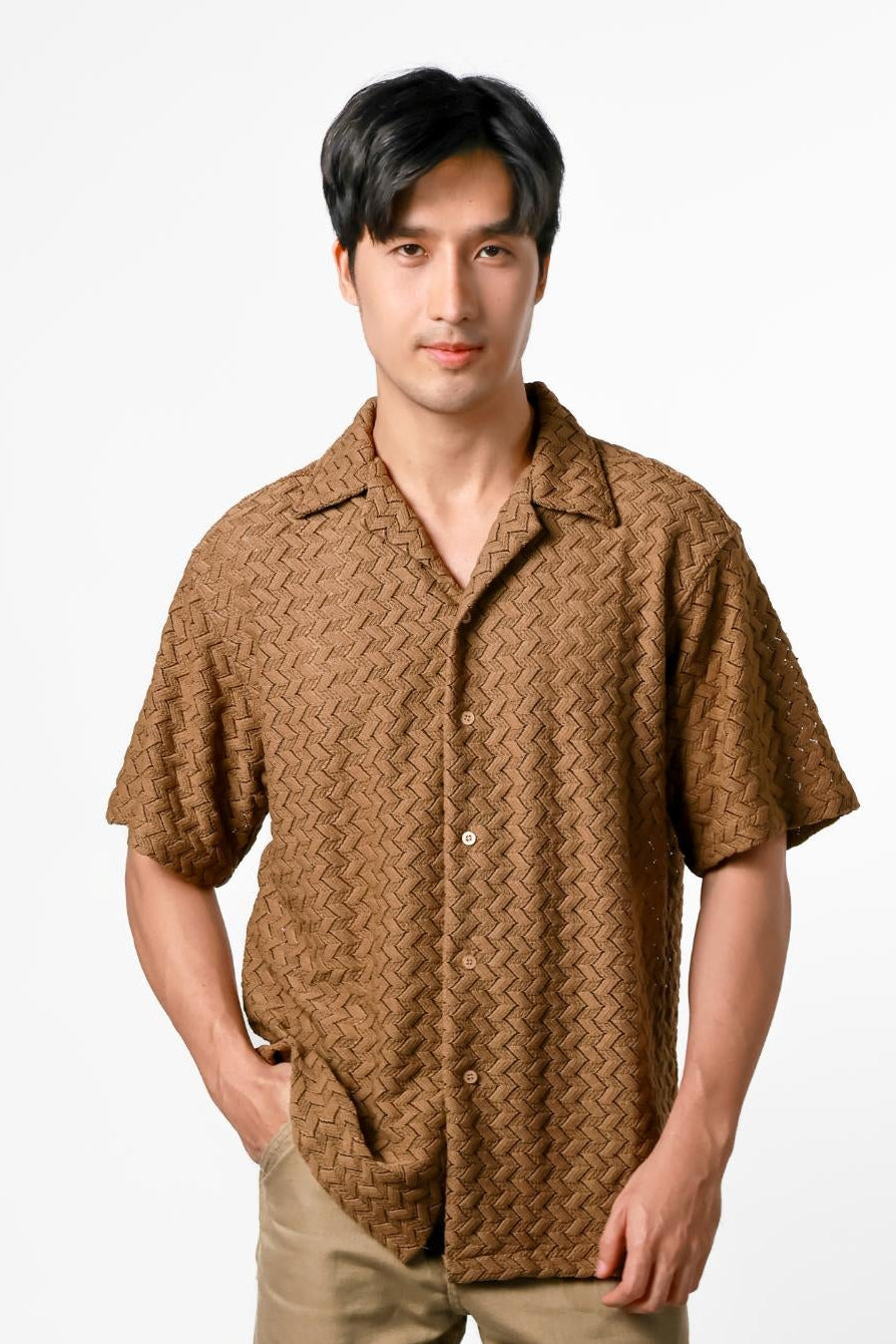 Man wearing a brown patterned shirt and beige pants on a white background