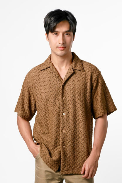 Man wearing a brown patterned shirt and beige pants on a white background