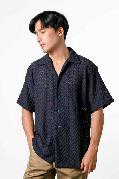 Man wearing a dark patterned shirt and beige pants on a white background