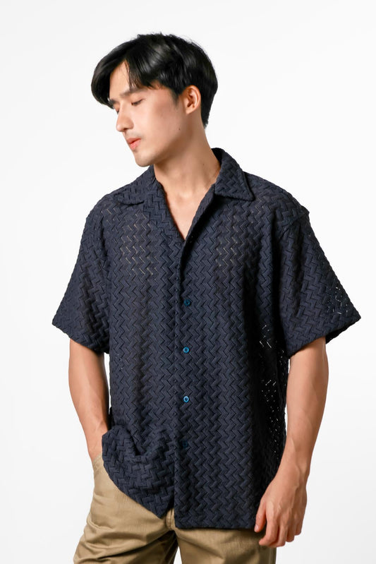 Man wearing a dark patterned shirt and beige pants on a white background